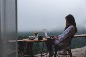A woman using and working on laptop computer while sitting on balcony with a beautiful nature view